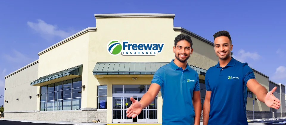 Two smiling Hispanic men stand outside in front of a Freeway Insurance office extending their hands in welcome.